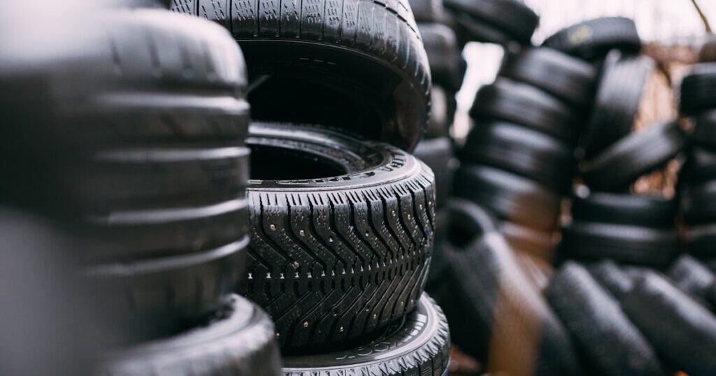 Stacks of black car tires are piled outdoors, with some tires standing upright and others laying on their sides.