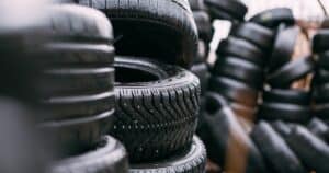 Stacks of black car tires are piled outdoors, with some tires standing upright and others laying on their sides.