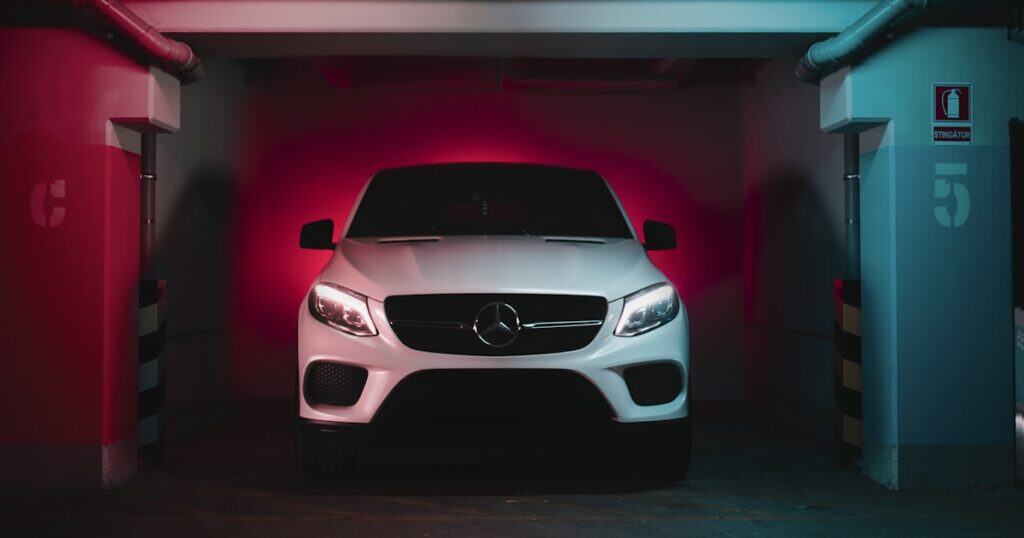 A white Mercedes-Benz SUV is parked in an indoor space with pink and blue lighting on the walls.